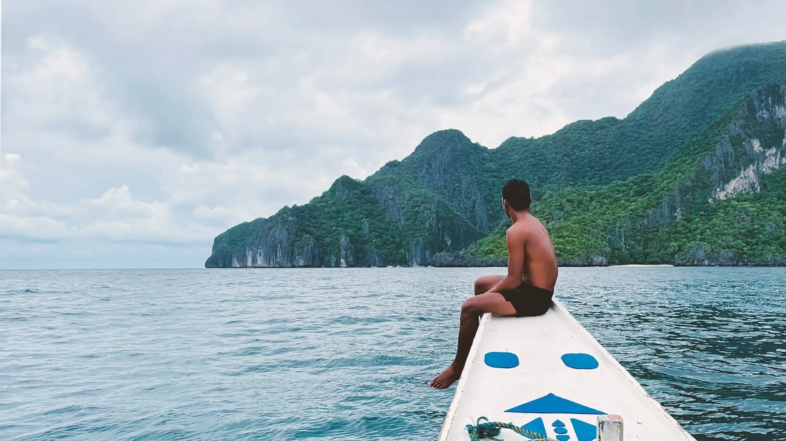 Filipino guide sitting on bow of boat during tour in El Nido