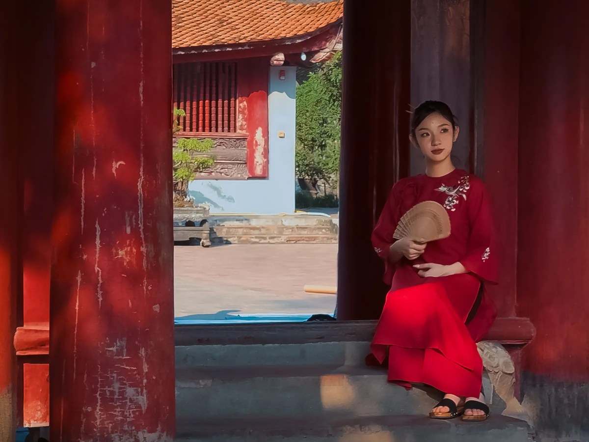 Young lady in traditional Vietnamese dress sitting with a fan by a courtyard