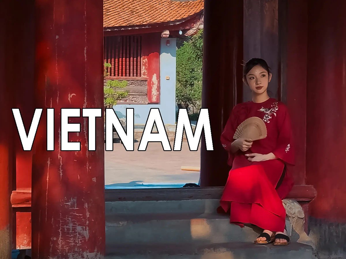 Young lady in traditional Vietnamese dress sitting with a fan by a courtyard